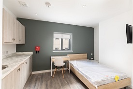 A studio room in 34 Park Street with a double bed on the right hand side, a desk with a chair against the back wall and a kitchen unit with cupboards and a sink in the left hand corner of the room.